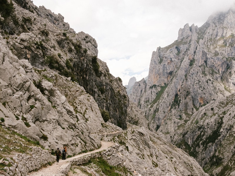 Two people walk the path of a rocky path in the Spanish mountains.